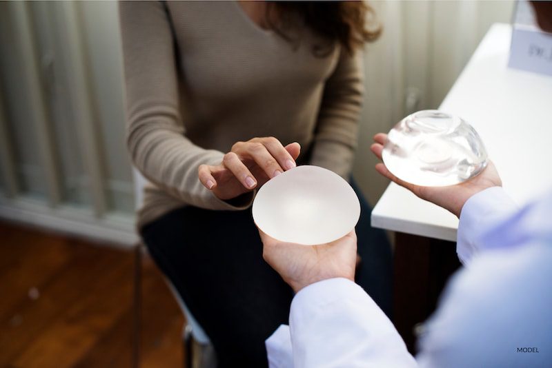 Woman touching two different breast implants, trying to select the right one for her.
