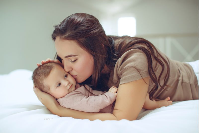 Young mother kissing her baby's cheek while lying on a bed