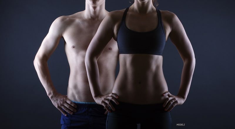 man and woman with toned midsections, standing with hands on hips