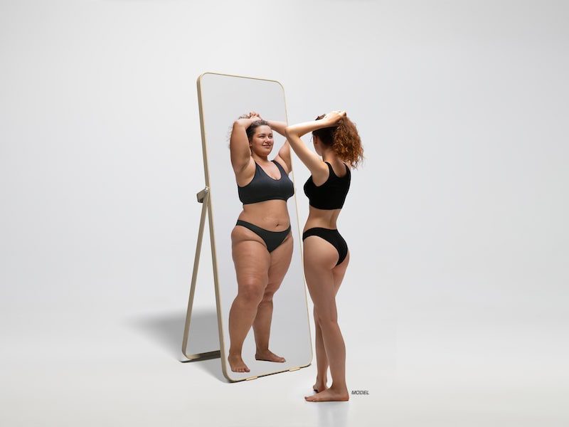 Woman standing in front of mirror showing herself before weight loss.