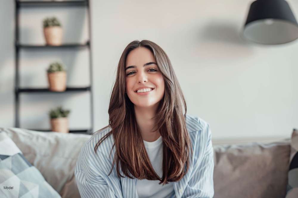 Young cheerful lady sitting on sofa, relaxing looking at the camera at home.