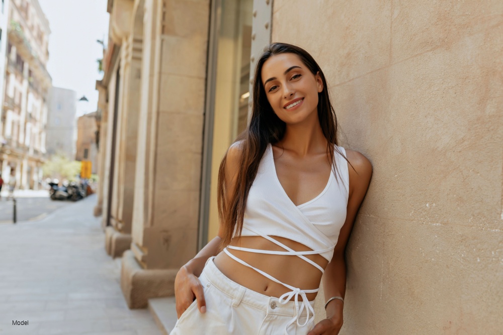 Woman smiliing with smooth skin leaning on a building wall outside in the city.